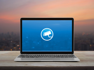 cctv camera flat icon with modern laptop computer on wooden table over blur of cityscape on warm light sundown, Business security and safety online concept