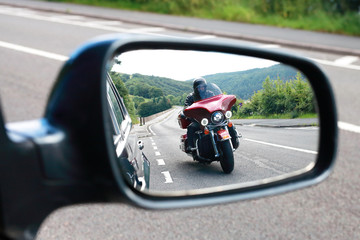 Biker riding motocycle seen by car driver in the mirror on english road