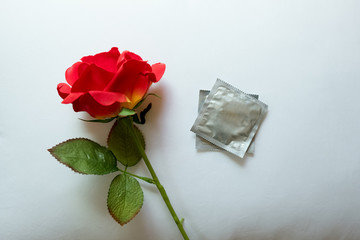 Condom and red rose on white pillow