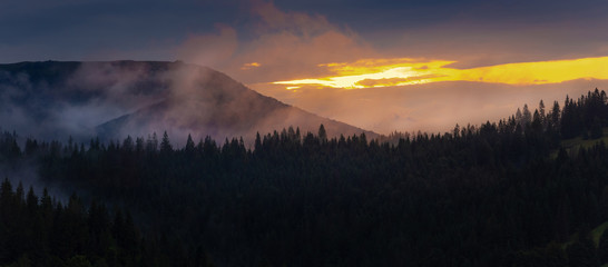 Bright sunset over foggy mountains. Vivid sun through the clouds over mountains slopes, covered with spruce forest. Carpathian mountains. Ukraine.