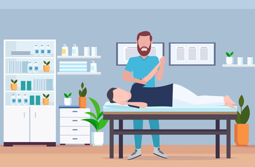 man patient lying on massage table therapist doing healing treatment massaging injured hand manual physical therapy rehabilitation concept full length modern hospital office interior horizontal