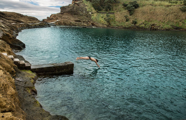 Headfirst into water, a man dives from a pier into the atlantic ocean. Islet of Vila Franca do Campo, Sao Miguel island, Azores