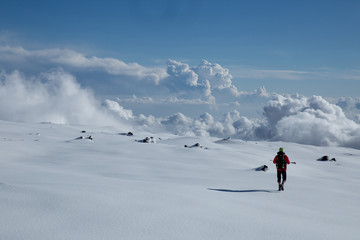 Man in shorts with small backpack walking on a snow leaving no trace. Cloudy blue color day on the glacier on the Etna volcano. Sicily, Italy