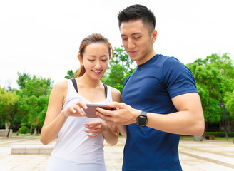 young fitness couple wearing sportswear and looking at smartphone