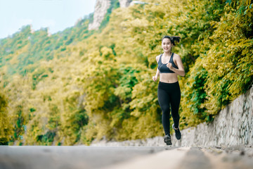Naklejka na ściany i meble An beautiful Asian woman running and listening music over road during moring. Workout and sport outdoor concept.