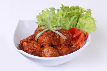 meatballs covered in spicy sauce decorated with tomato lettuce and leeks. on white background