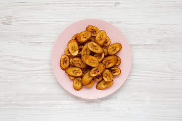 Homemade fried plantains on a pink plate over white wooden background, top view. Flat lay, overhead, from above.