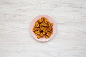 Homemade fried plantains on a pink plate over white wooden surface, top view. Flat lay, overhead, from above.