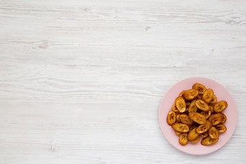 Fototapeta na wymiar Homemade fried plantains on a pink plate over white wooden background, overhead view. Flat lay, top view, from above. Copy space.