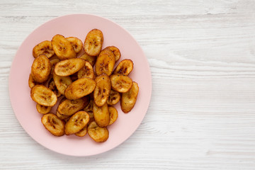 Homemade fried plantains on a pink plate over white wooden background, top view. Flat lay, overhead, from above. Copy space.