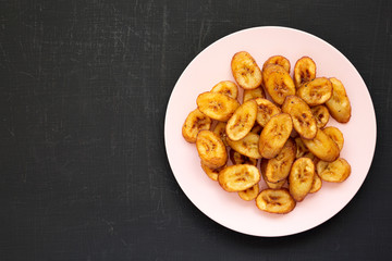 Homemade fried plantains on a pink plate on a black surface, overhead view. Flat lay, from above, top view. Copy space.