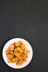 Homemade fried plantains on a pink plate on a black background, top view. Flat lay, from above, overhead. Copy space.