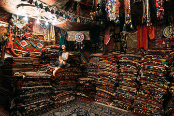Girl in a carpet store. Happy woman customer choosing colored carpet in carpet store. Girl in Turkish market with amazing colorful carpets. Cheerful woman customer shopping carpet in interior store