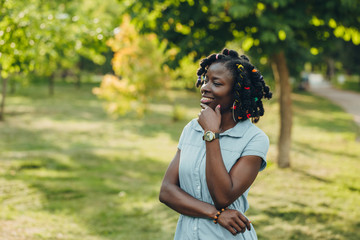 Portrait of a African beauty smiling young black woman in a park with sunlight flare and copy space