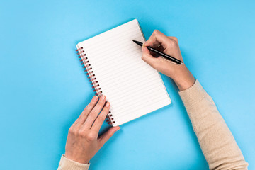 Woman's hands with perfect manicure holding pencil and  notepad as mockup for your design. blue background, flat lay style.