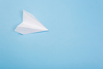 Flat lay of white paper airplane and blank paper on blue background.