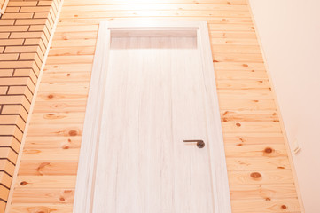 Interior with a combination of white wooden doors, beige decorative brick and wooden lining of pine
