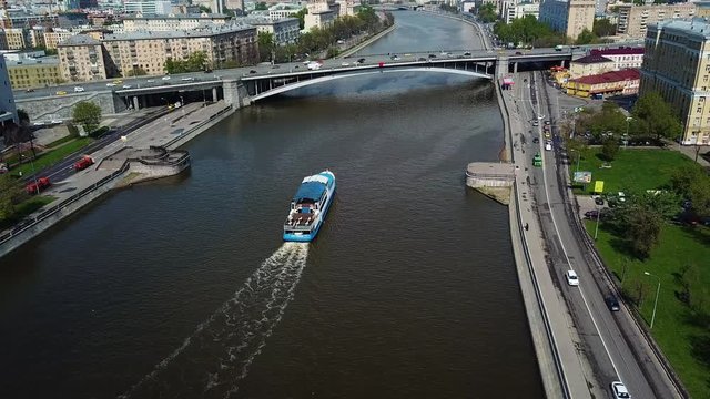 Pleasure boat float or going down the river in city or megapolis. Aerial view of blue and white boat with people. Boat is going under the bridge.