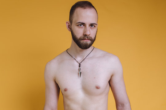 bearded man with a bare torso posing on a colored background. skinny guy after exercise and diet. emotional portrait of a student. man with a pendant around his neck