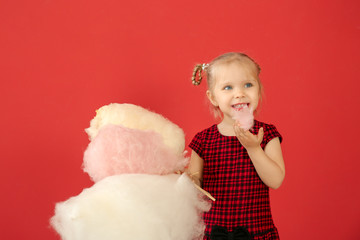 Cute little girl with cotton candy on color background