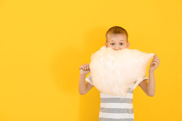Cute little boy with cotton candy on color background