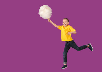 Jumping little boy with cotton candy on color background