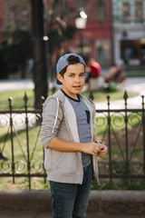 Stylish little school boy in blue cap posing outside for photo. Boy walking in the city in sping summer weather