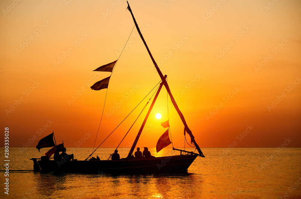 Wall mural tourists sail in a traditional boat and enjoy the colorful sunset on the island of zanzibar,tanzania - Wall murals