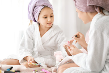 Obraz na płótnie Canvas Mother and her little daughter in bathrobes manicuring nails in bedroom