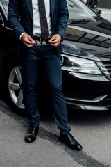 cropped view of african american man in suit holding sunglasses near car