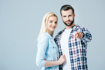 beautiful smiling young woman near man pointing with finger isolated on grey