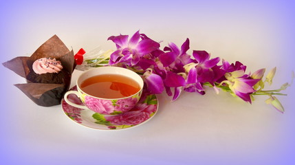 Obraz na płótnie Canvas A beautiful cup of tea on a saucer, a cupcake, a sprig of flowers (phalaenopsis)