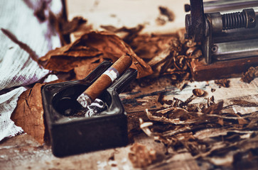 close up of a Cuban cigar and a black ceramic ashtray on the wooden table whit dried and cured...