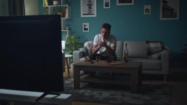 Man is resting at home on the couch at night, smokes and watching TV