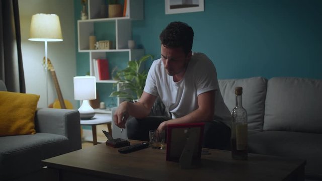 Sad man looking at photo of ex-girlfriend, smoke and drink alcohol