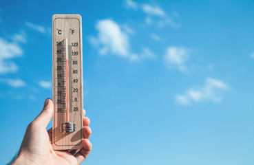 Hand holding thermometer on blue sky background.