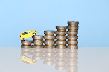 Miniature yellow car model on growing stack of coins money on blue background, Saving money for car, Finance and car loan, Investment and business concept
