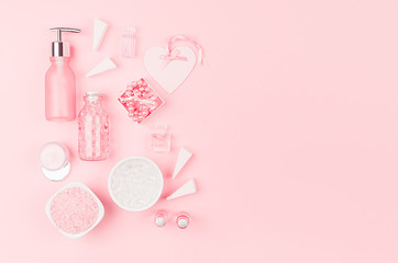 Cosmetic products and accessories in pink color - cream, bath salt, essential oil, soap, towel,  pearls, bottles, heart, bowl on pink background, top view.