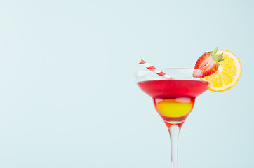 Homemade tropical fruit cocktail  with red and yellow liquor, orange slice, strawberry, straw in fresh mint color background, closeup, details, top.