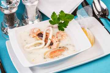 Cheese creamy fish, chicken soup with squid rings according to a Mediterranean recipe on a blue background