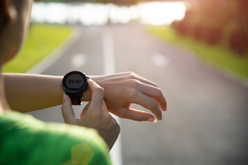 Young fitness woman runner setting up smart watch before running training during sunset. Outdoor...