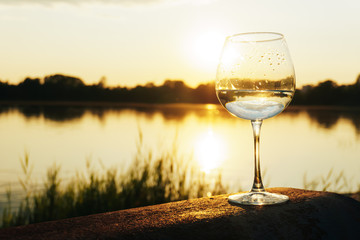 a glass of water on the background of the river and the sunset