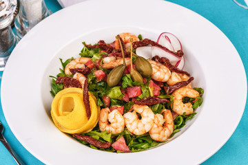 Mediterranean salad. Arugula, tomatoes, shrimps, olives, olives, basil and rosemary, dressed with olive oil and balsamic sauce, decorated with lemon and chili pepper
