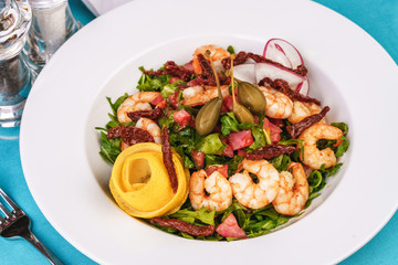 Mediterranean salad. Arugula, tomatoes, shrimps, olives, olives, basil and rosemary, dressed with olive oil and balsamic sauce, decorated with lemon and chili pepper