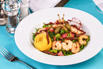 Mediterranean salad. Arugula, tomatoes, shrimps, olives, olives, basil and rosemary, dressed with olive oil and balsamic sauce, decorated with lemon and chili pepper