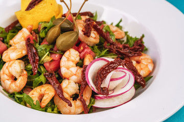 Mediterranean salad. Arugula, tomatoes, shrimps, olives, olives, basil and rosemary, dressed with olive oil and balsamic sauce, decorated with lemon and chili pepper