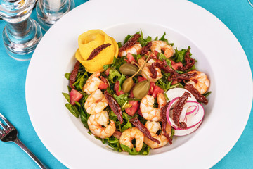 Mediterranean salad. Arugula, tomatoes, shrimps, olives, olives, basil and rosemary, dressed with olive oil and balsamic sauce, decorated with lemon and chili pepper