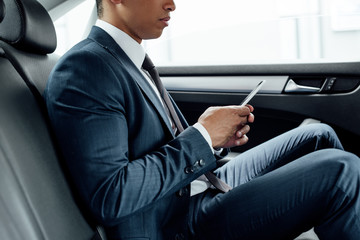 partial view of african american businessman using smartphone in car