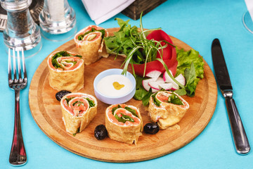 Mediterranean snack. Rolls with salmon, greens, cucumber and vegetables with cream sauce