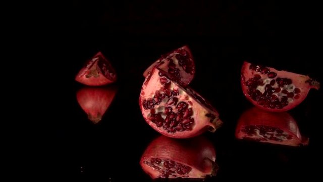 Fresh red pomegranate split into parts. slow motion. Black background. Fall into pieces